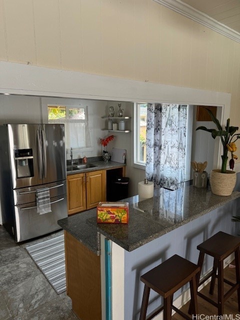 kitchen featuring a breakfast bar area, dark stone counters, ornamental molding, sink, and stainless steel fridge with ice dispenser