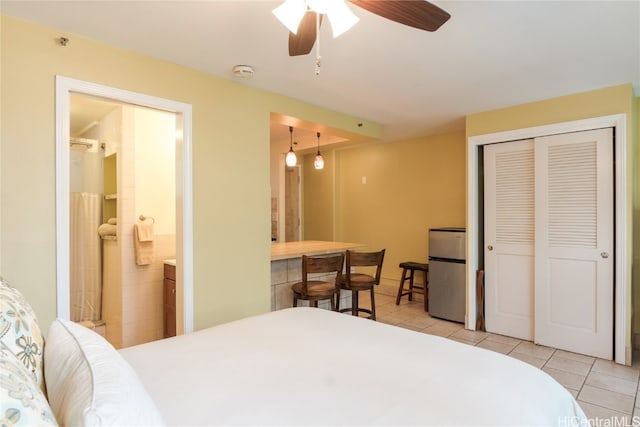 bedroom featuring ensuite bathroom, light tile patterned flooring, a closet, ceiling fan, and stainless steel refrigerator