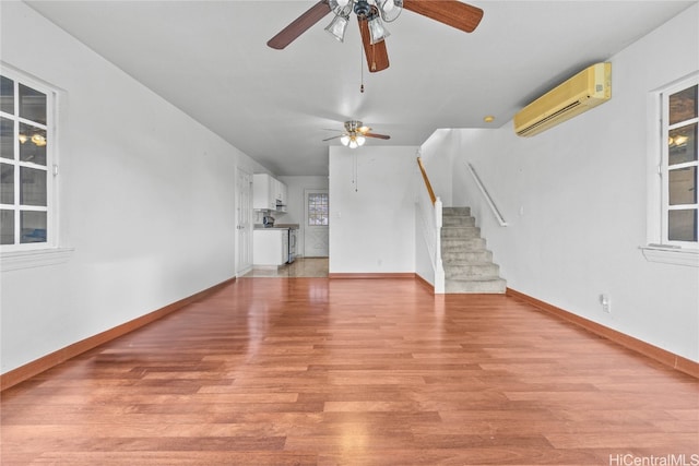 unfurnished living room with a wall mounted air conditioner, ceiling fan, and light hardwood / wood-style floors