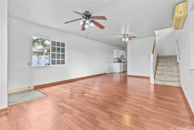 unfurnished living room with a wall unit AC, light wood-type flooring, and ceiling fan