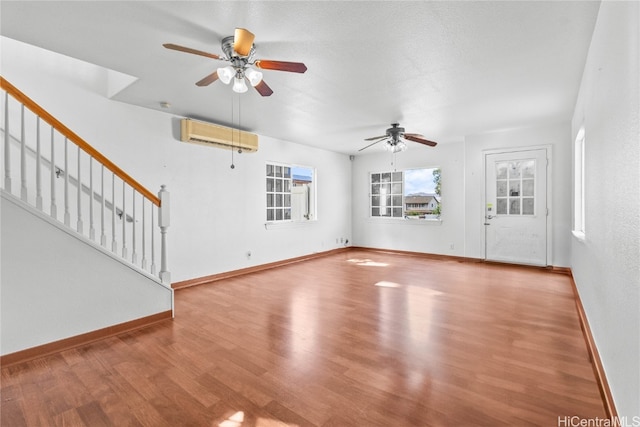 unfurnished living room featuring ceiling fan, hardwood / wood-style flooring, a textured ceiling, and a wall unit AC