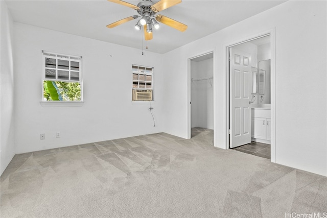 unfurnished bedroom with dark colored carpet, a closet, a walk in closet, ensuite bath, and ceiling fan