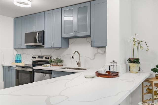 kitchen featuring kitchen peninsula, appliances with stainless steel finishes, tasteful backsplash, light stone counters, and sink