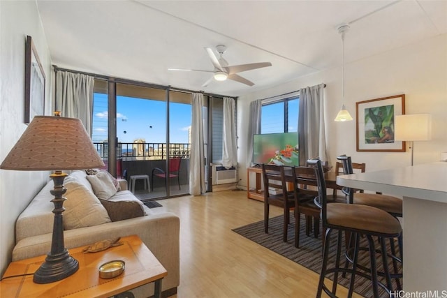 living room featuring ceiling fan, light hardwood / wood-style floors, and a wall of windows