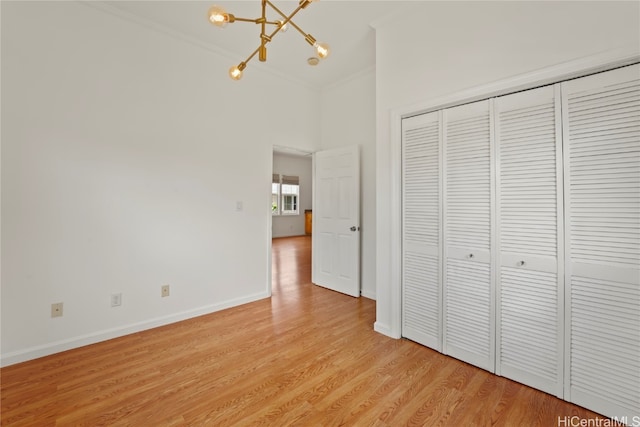 unfurnished bedroom featuring an inviting chandelier, crown molding, a closet, and light wood-type flooring