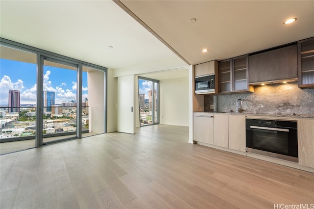 kitchen featuring oven, light hardwood / wood-style flooring, built in microwave, a wall of windows, and tasteful backsplash