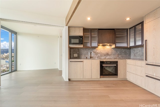 kitchen with oven, black microwave, tasteful backsplash, light wood-type flooring, and sink