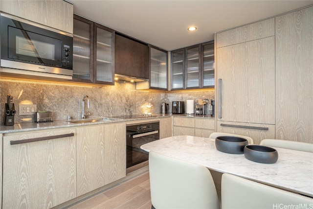 kitchen with light stone countertops, sink, backsplash, light hardwood / wood-style floors, and stainless steel appliances