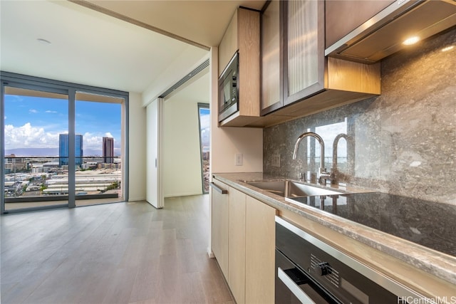 kitchen featuring stainless steel microwave, sink, decorative backsplash, light hardwood / wood-style flooring, and exhaust hood