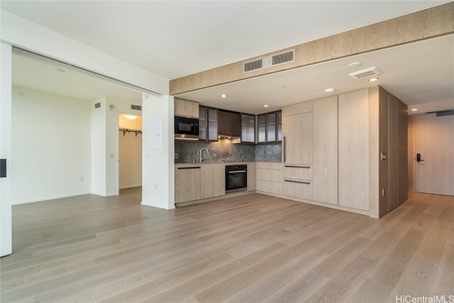 kitchen featuring stainless steel microwave, oven, light wood-type flooring, light brown cabinetry, and tasteful backsplash