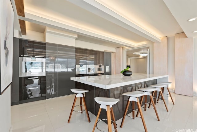 kitchen with light tile patterned flooring, a breakfast bar area, a large island, and light stone counters