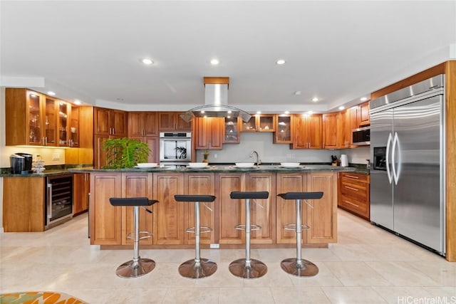 kitchen with a kitchen breakfast bar, appliances with stainless steel finishes, beverage cooler, and a center island with sink