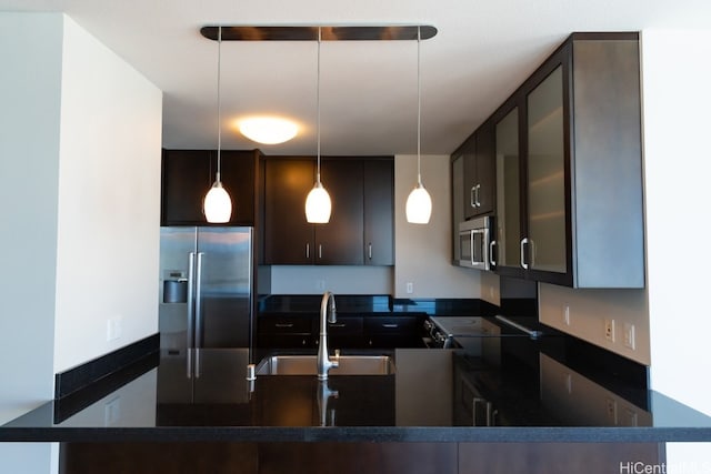 kitchen featuring kitchen peninsula, stainless steel appliances, dark brown cabinets, sink, and decorative light fixtures