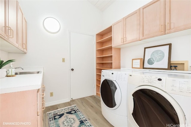 clothes washing area with cabinets, sink, washer and dryer, and light hardwood / wood-style flooring