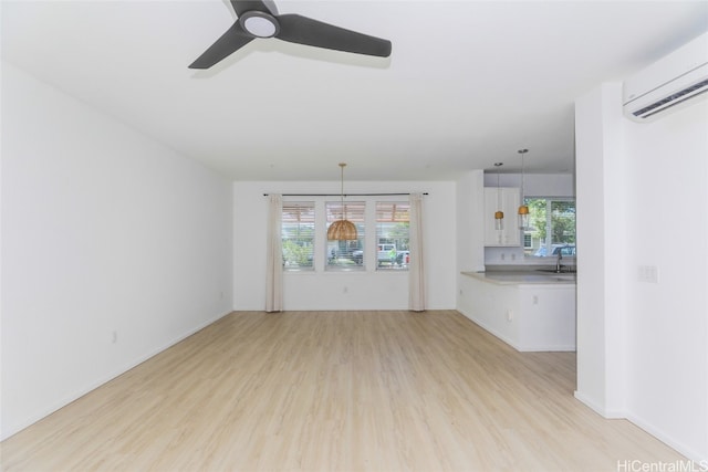 unfurnished living room with ceiling fan, an AC wall unit, sink, and light wood-type flooring