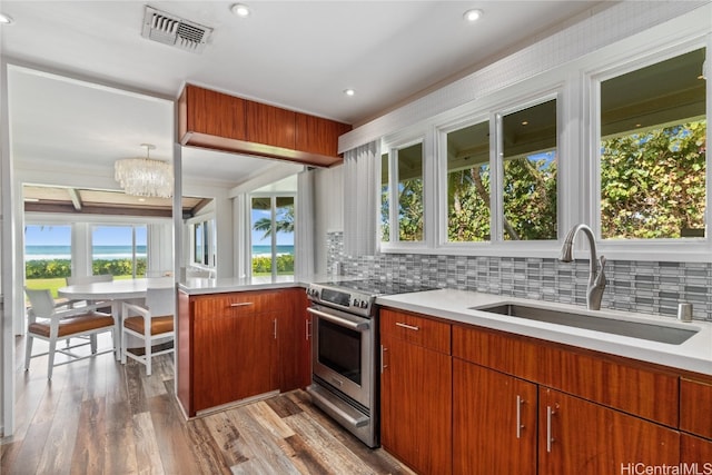 kitchen with a healthy amount of sunlight, electric range, light wood-type flooring, sink, and decorative light fixtures