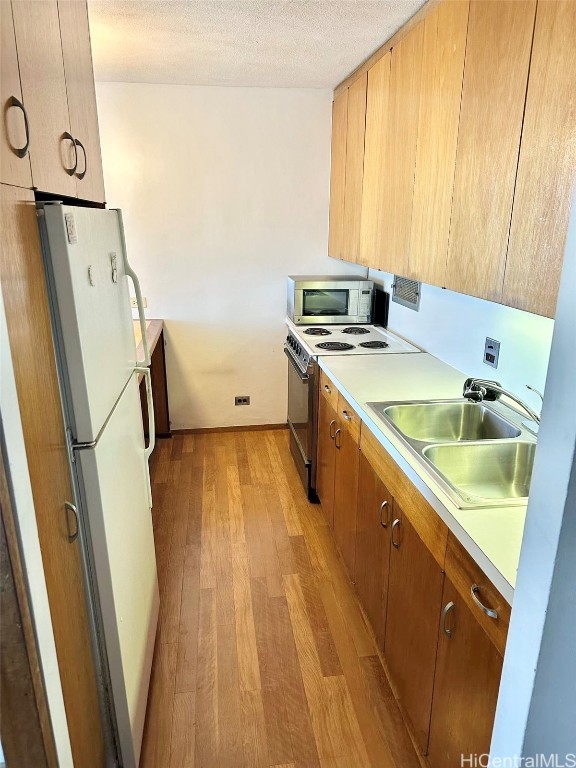 kitchen with white appliances, a textured ceiling, light hardwood / wood-style flooring, and sink