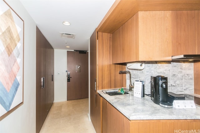 kitchen with light tile patterned floors, tasteful backsplash, light stone countertops, and sink