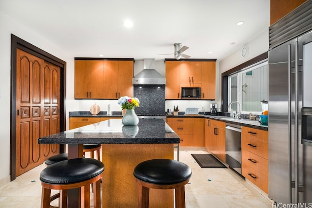 kitchen with wall chimney range hood, a kitchen island, ceiling fan, stainless steel appliances, and a breakfast bar