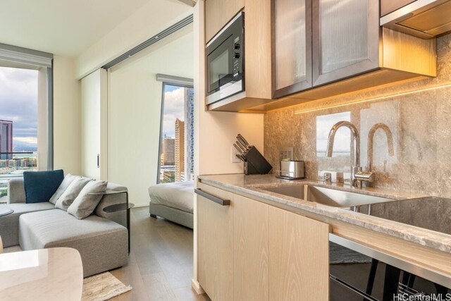 kitchen with light brown cabinets, decorative backsplash, built in microwave, light hardwood / wood-style floors, and sink