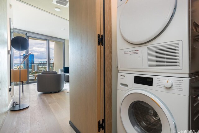 clothes washing area with stacked washer / dryer and light hardwood / wood-style flooring