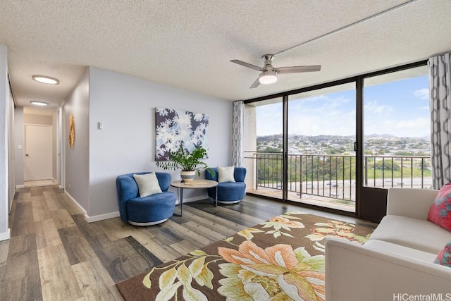 sitting room with floor to ceiling windows, a textured ceiling, baseboards, and wood finished floors