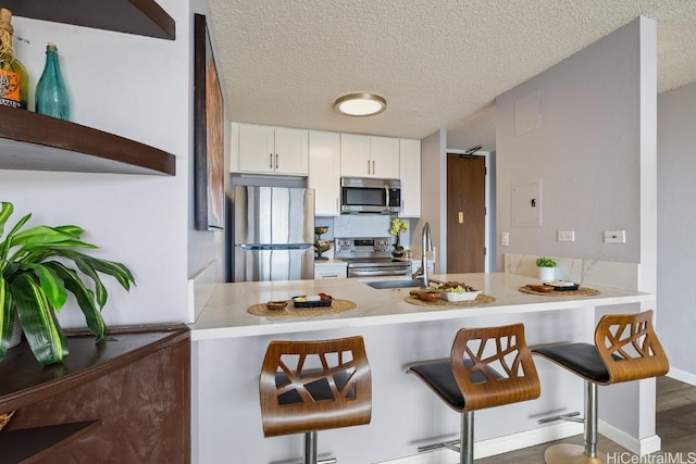 kitchen featuring stainless steel appliances, white cabinetry, a peninsula, and a kitchen bar