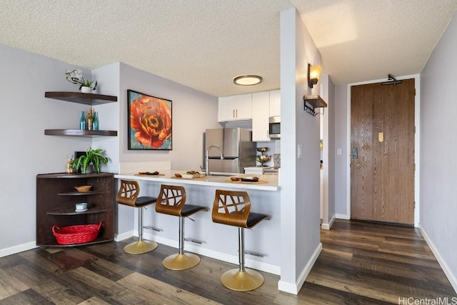 kitchen with a peninsula, white cabinets, appliances with stainless steel finishes, dark wood-style floors, and a kitchen bar