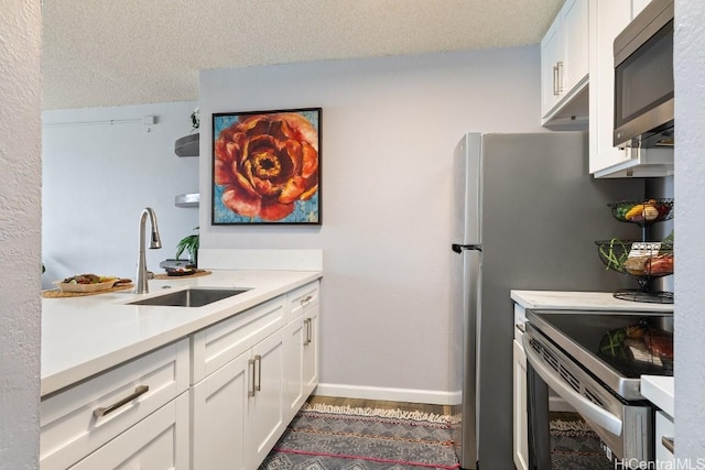 kitchen featuring white cabinets, stainless steel appliances, a textured ceiling, light countertops, and a sink