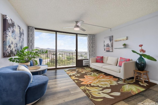 living area with a textured ceiling, ceiling fan, a wall of windows, and wood finished floors