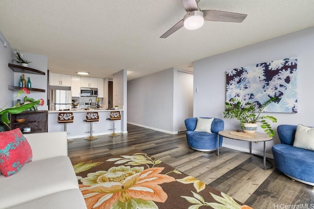 living room with ceiling fan, a textured ceiling, baseboards, and wood finished floors