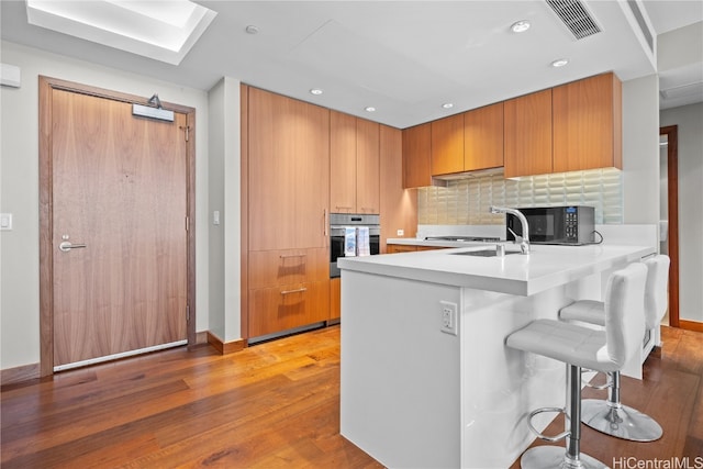 kitchen with kitchen peninsula, hardwood / wood-style floors, backsplash, stainless steel oven, and a breakfast bar