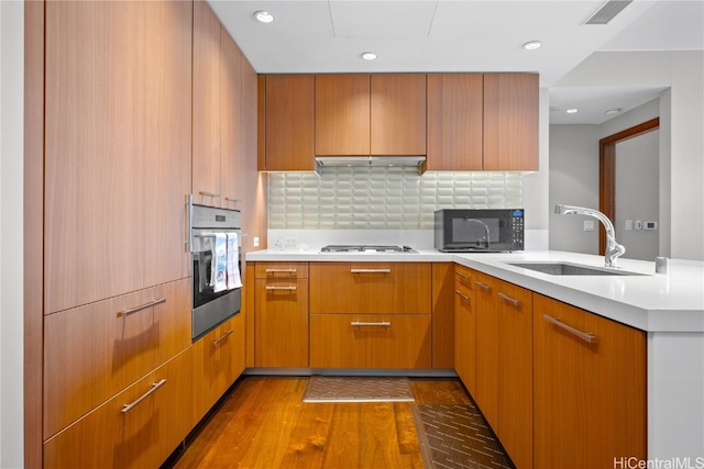 kitchen with wood-type flooring, sink, stainless steel oven, white gas cooktop, and decorative backsplash