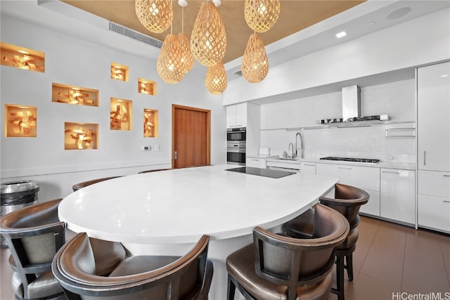 kitchen with double oven, black electric cooktop, range hood, pendant lighting, and white cabinetry