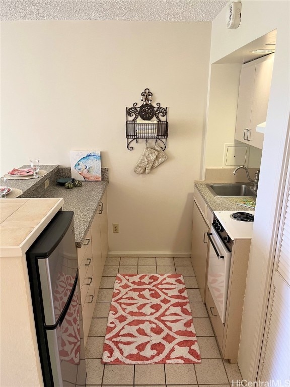 kitchen with sink, a textured ceiling, light tile patterned floors, stainless steel refrigerator, and white electric stove