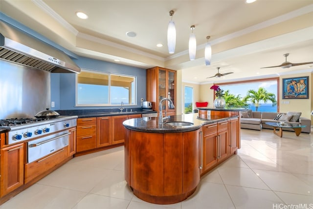 kitchen with hanging light fixtures, a center island with sink, ornamental molding, wall chimney exhaust hood, and sink