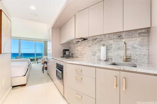 kitchen with oven, decorative backsplash, light stone counters, sink, and a water view