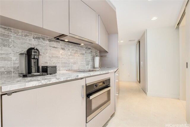 kitchen featuring range hood, backsplash, light stone countertops, white cabinets, and appliances with stainless steel finishes