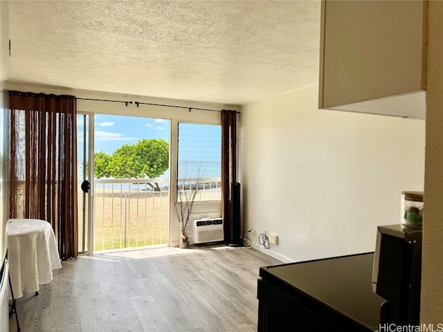 interior space with a water view, a textured ceiling, light wood-type flooring, and a wall unit AC