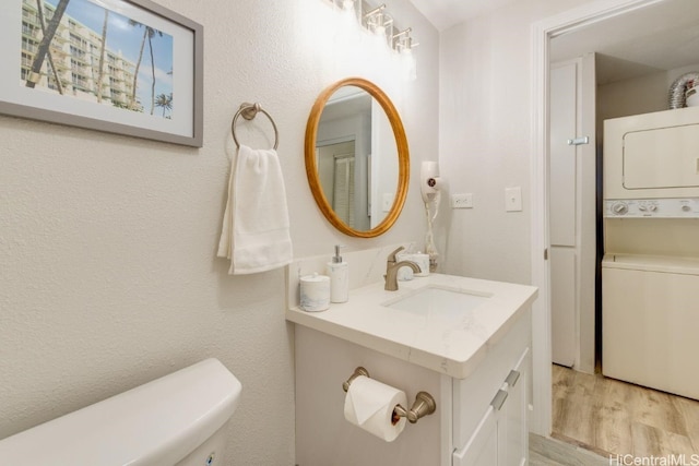 bathroom featuring toilet, hardwood / wood-style flooring, stacked washer and dryer, and vanity