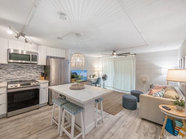 kitchen featuring appliances with stainless steel finishes, light wood-type flooring, a center island, white cabinets, and a breakfast bar