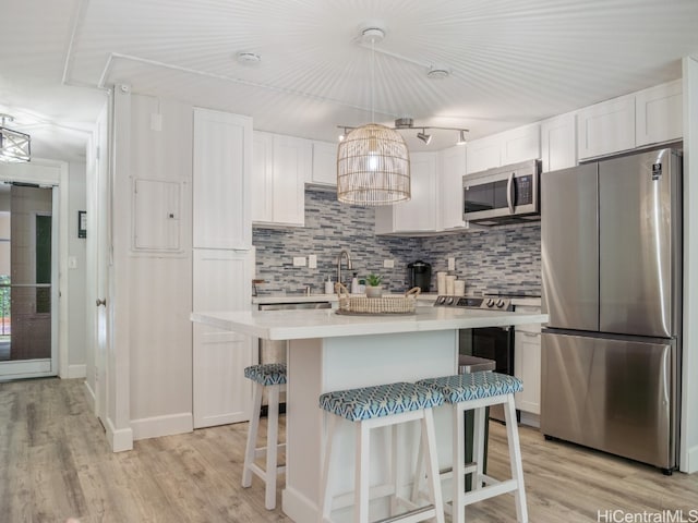 kitchen featuring light wood-type flooring, stainless steel appliances, pendant lighting, white cabinets, and decorative backsplash