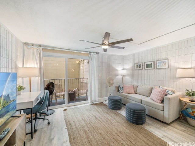 living room with tile walls, light wood-type flooring, and ceiling fan