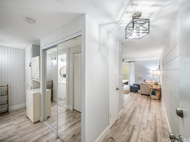 corridor with stacked washer / dryer, tile walls, and light hardwood / wood-style flooring