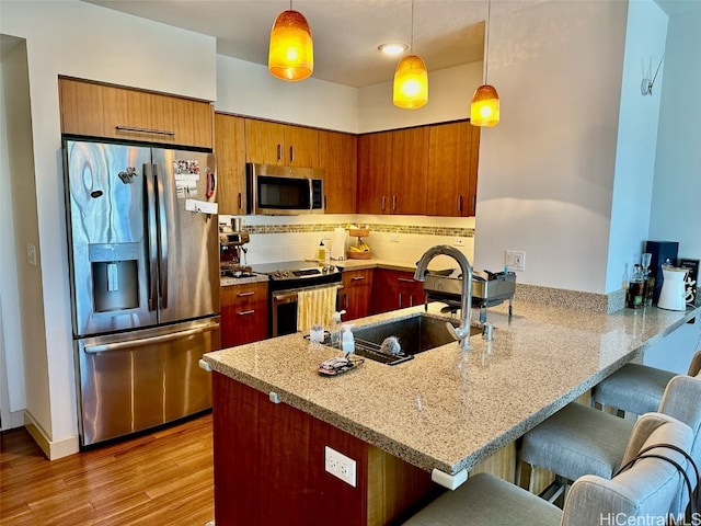 kitchen featuring light wood-type flooring, appliances with stainless steel finishes, kitchen peninsula, and hanging light fixtures