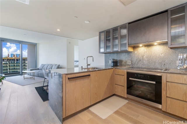 kitchen with sink, stainless steel oven, kitchen peninsula, and light wood-type flooring