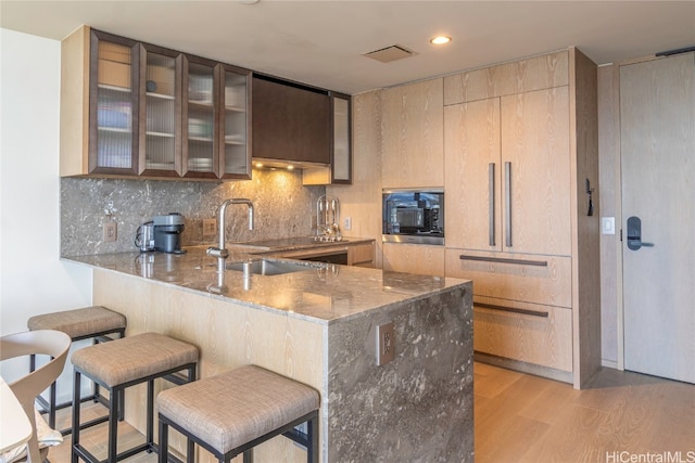 kitchen with kitchen peninsula, a breakfast bar area, stainless steel microwave, light hardwood / wood-style floors, and sink