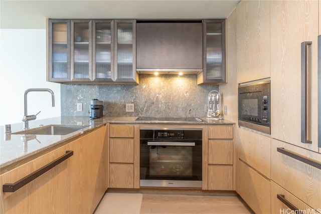 kitchen featuring decorative backsplash, light stone countertops, black appliances, light hardwood / wood-style floors, and sink