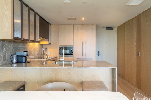 kitchen with decorative backsplash, a kitchen breakfast bar, kitchen peninsula, light stone countertops, and light wood-type flooring