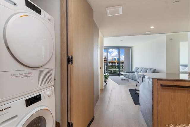 laundry room with light hardwood / wood-style flooring and stacked washer and clothes dryer